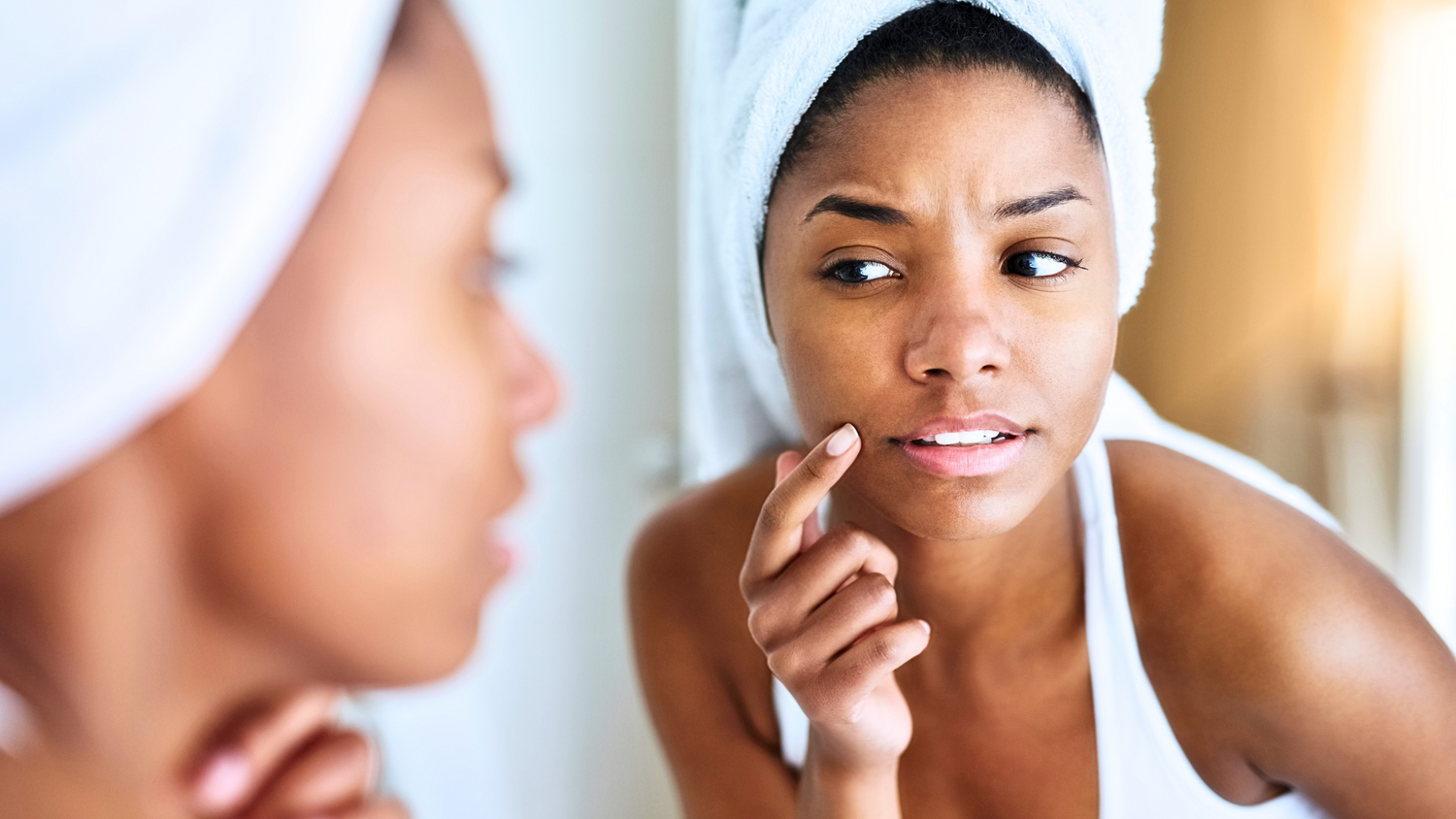 A female looking the mirror at a breakout due to skin urging during the acclimation phase of her new active skincare routine.