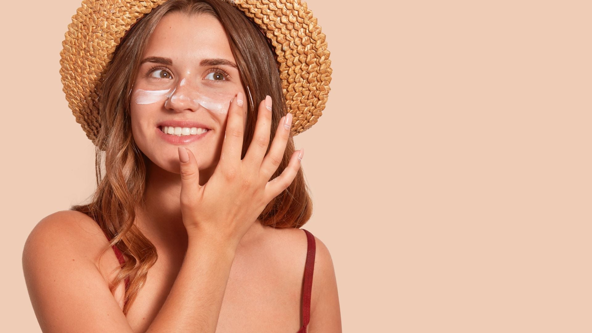 Young woman wearing straw hat with glow of sunshine on her face, applying sunscreen for sun protection.