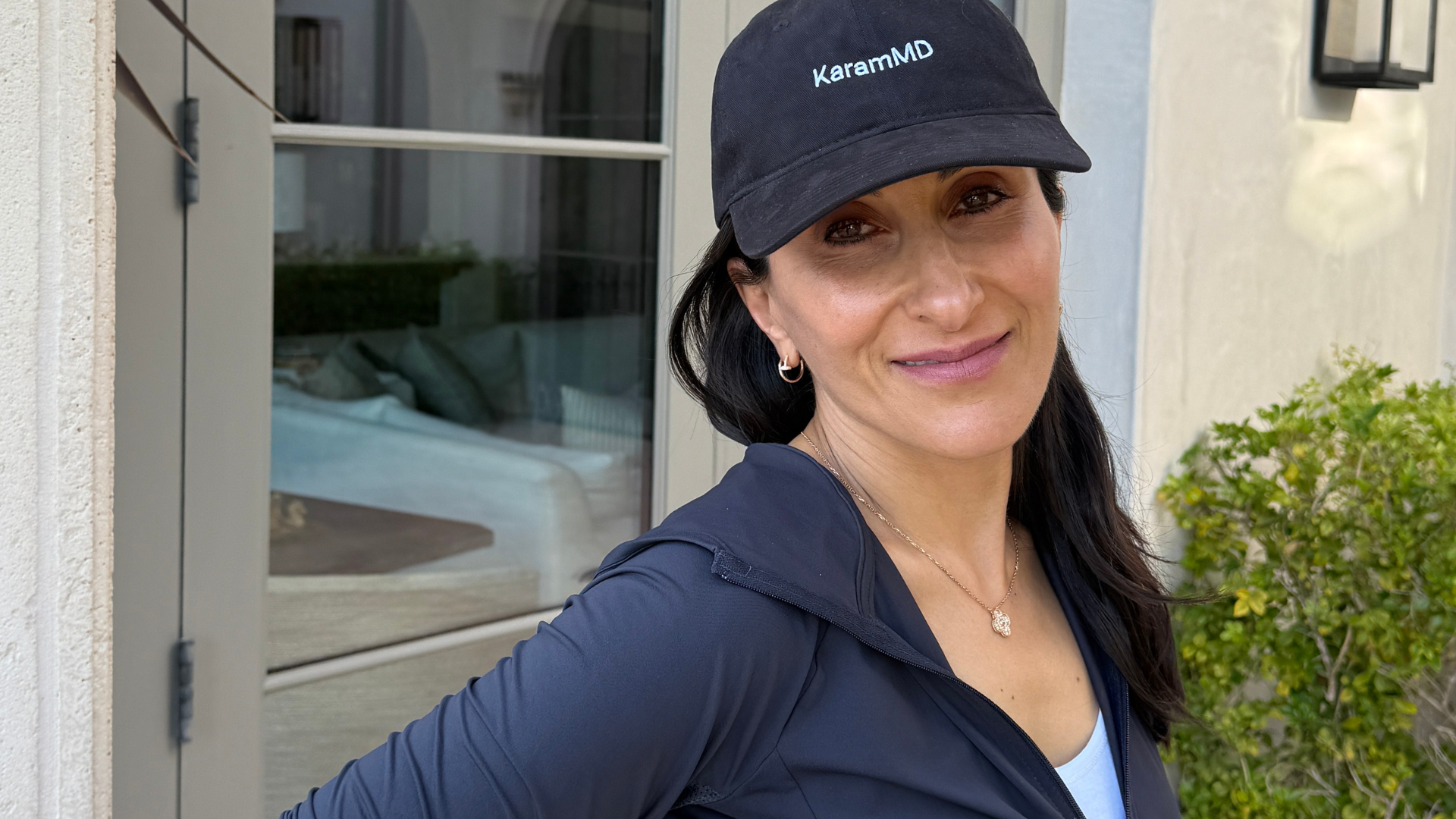 Neda Karam, Dr. Amir Karam's wife, posing with natural beauty and ease, outside in a KaramMD hat