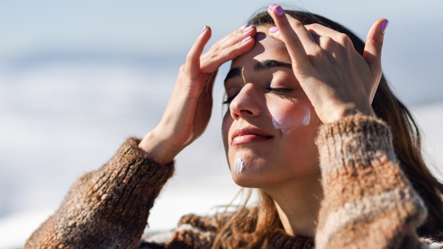 woman in sweater and cloudy weather applying  sunscreen