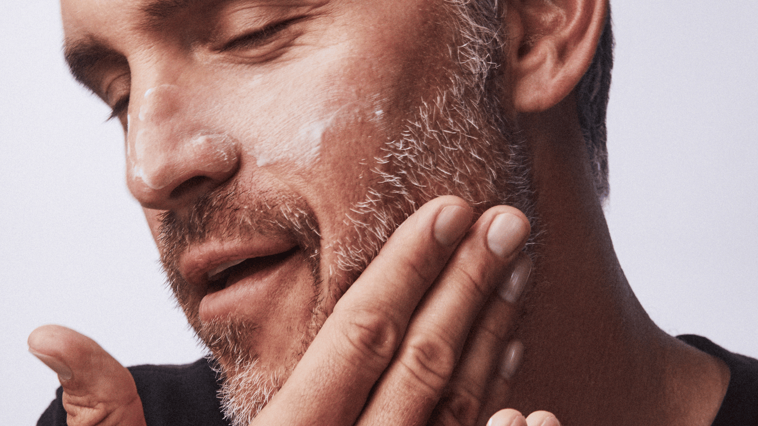 Man massaging skincare cream into his cheek and beard area.