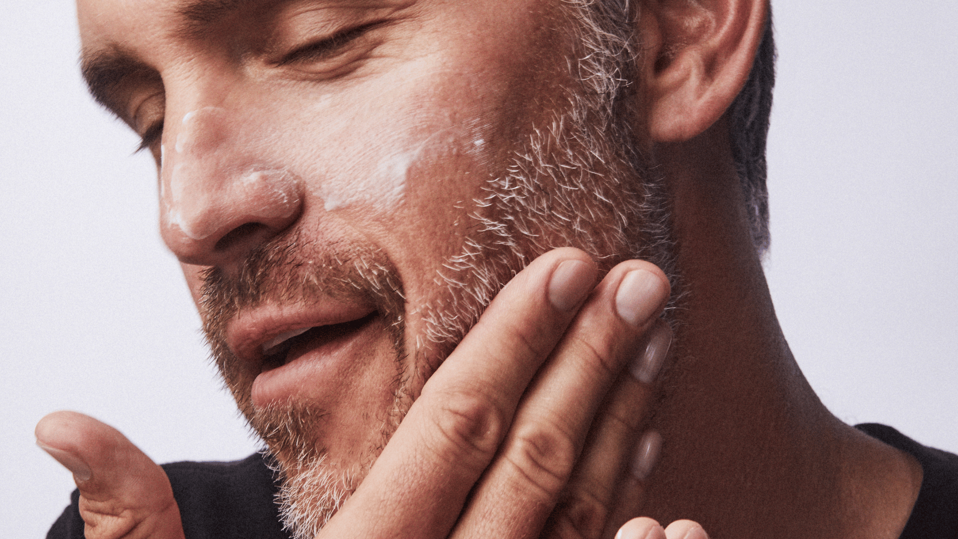 Man massaging skincare cream into his cheek and beard area.