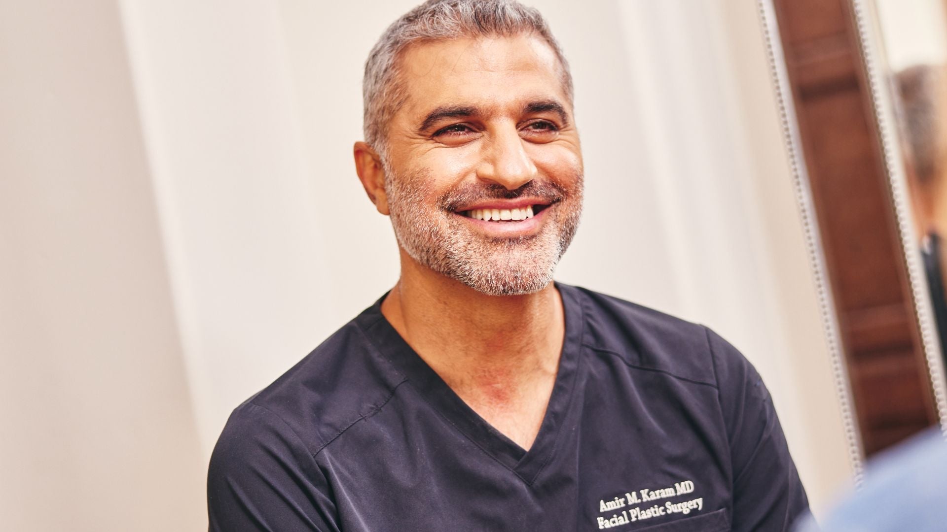 Dr. Amir Karam smiling in black medical scrubs during a patient consultation.