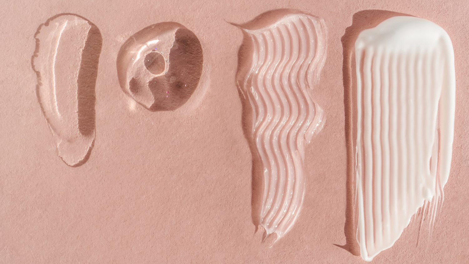 Skincare product textures swatched on a pink background, showing gel, serum, cream, and exfoliating formulas.