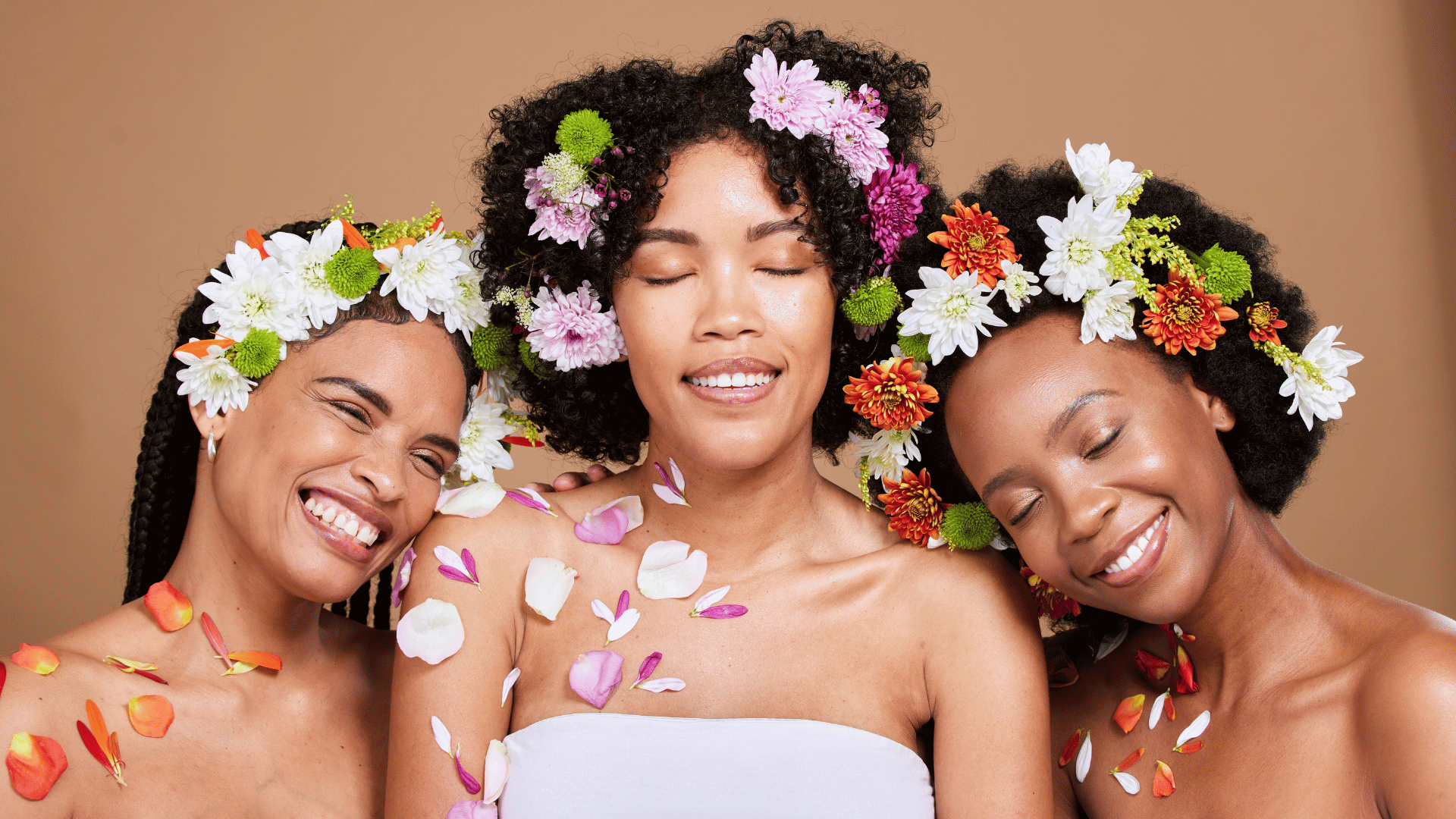 three women glowing with confidence and beautiful skin with flowers in their hair and petals on their skin for spring