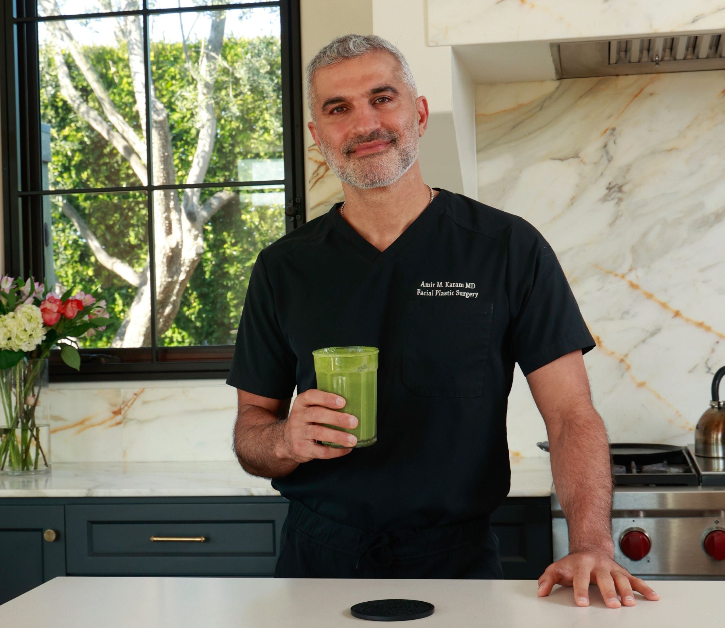Dr. Karam holding a green drink in a modern kitchen