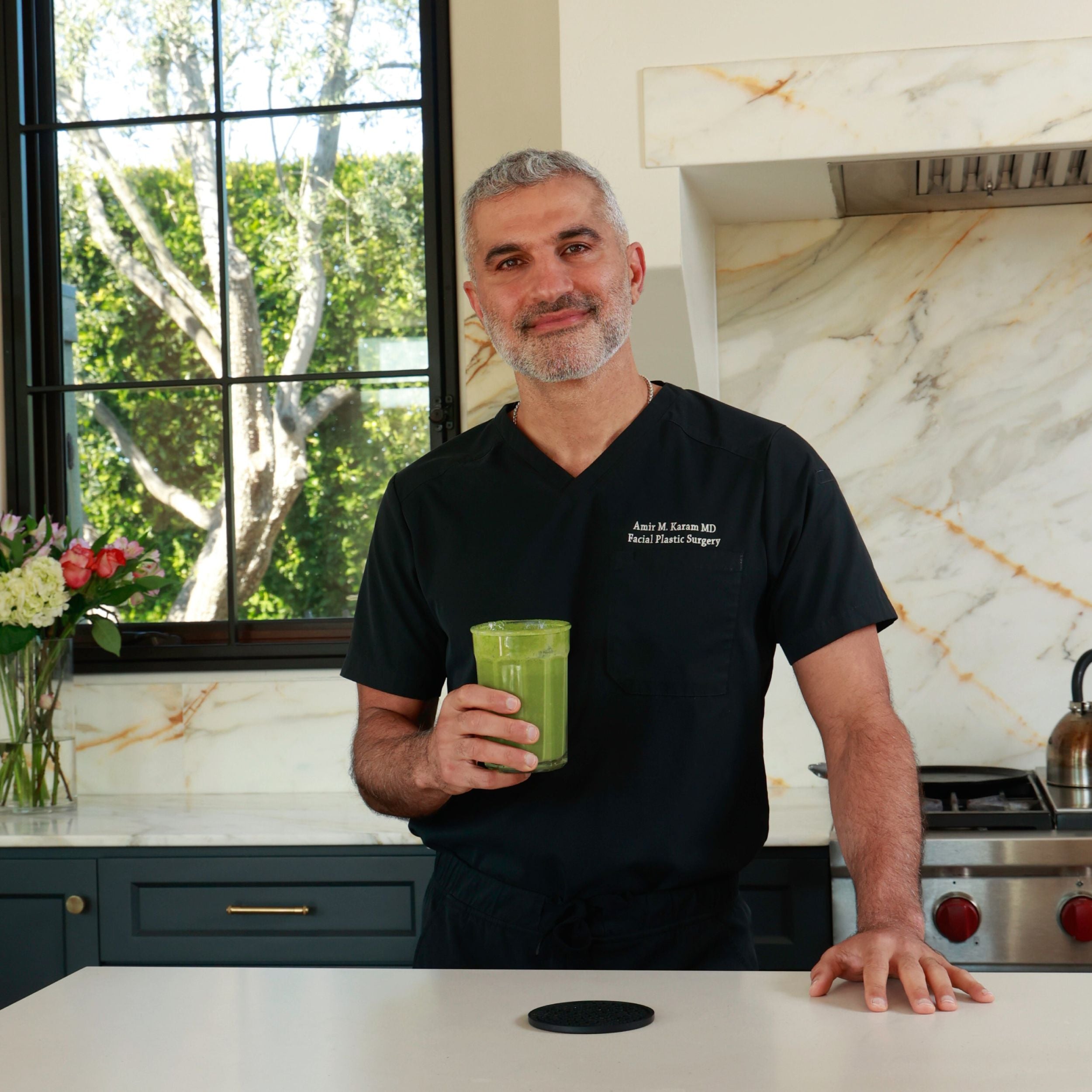 Dr. Karam holding a green drink in a modern kitchen