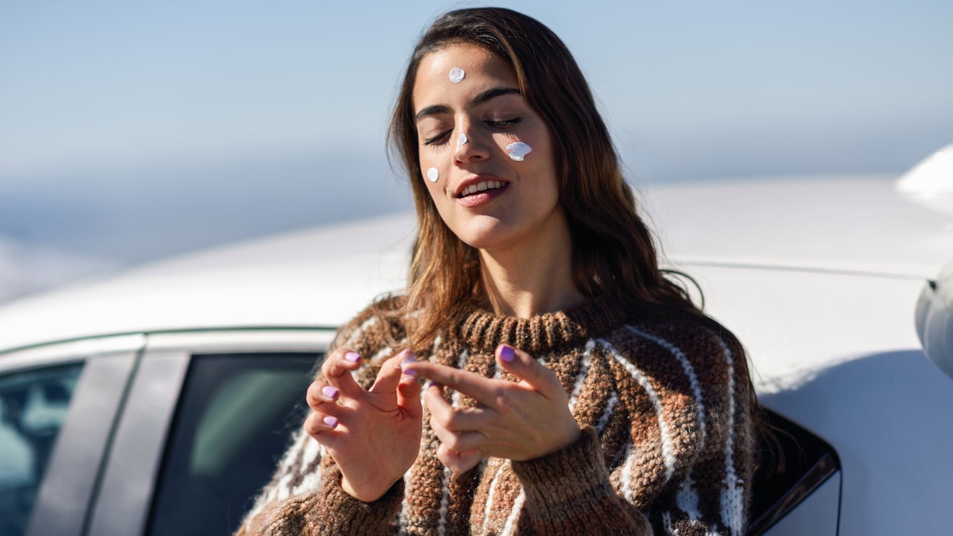 woman in sweater and cloudy weather applying  sunscreen