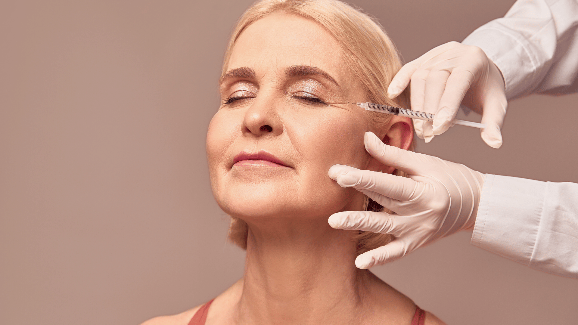 Mature woman receiving a facial injectable treatment from a gloved skincare professional.