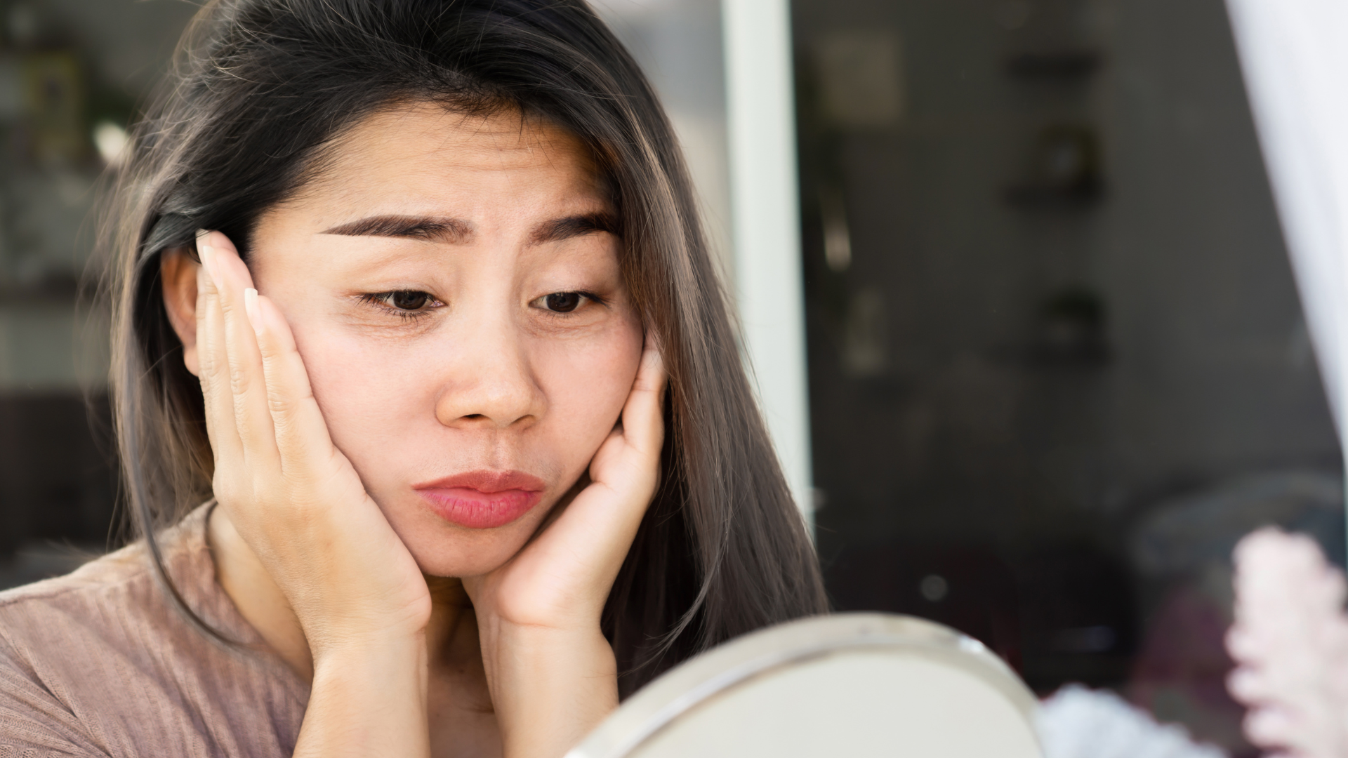 Woman with tired-looking eyes. Hands placed on face in frustration. 