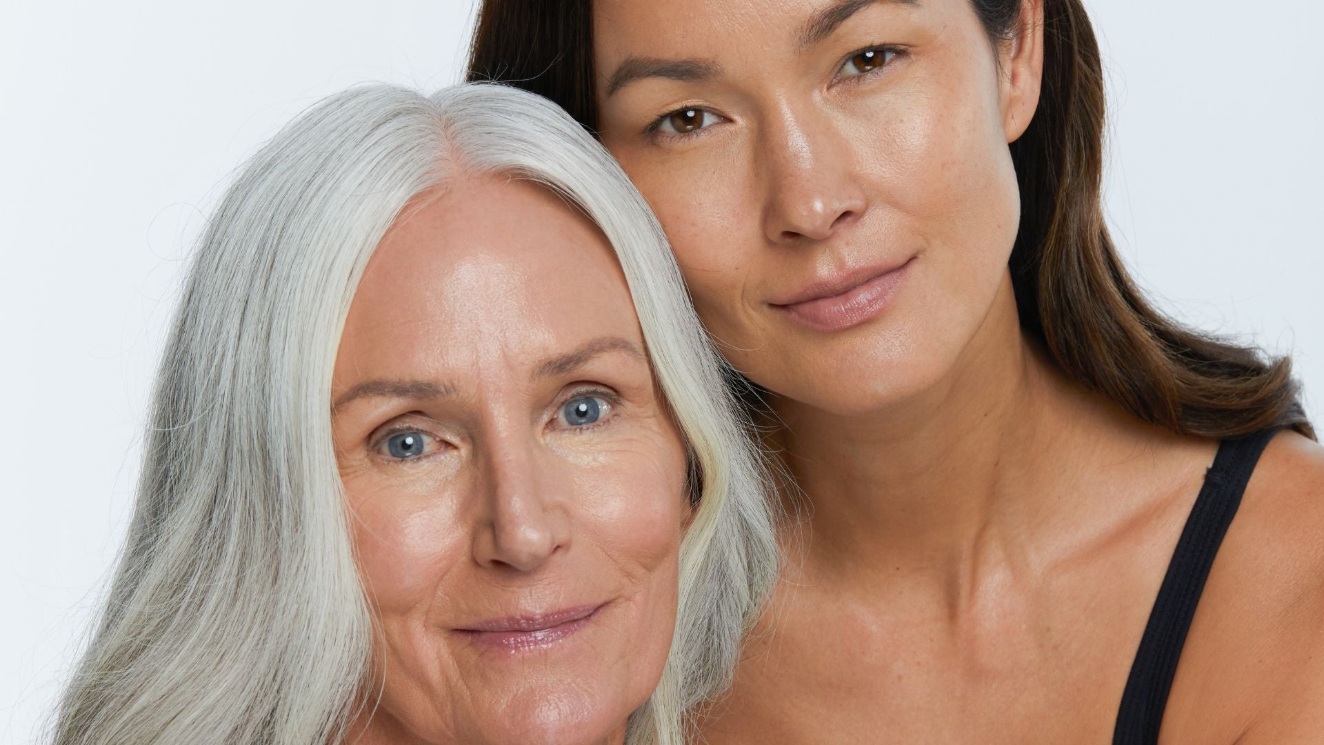 Two women of different ages posing closely together with natural, glowing skin.